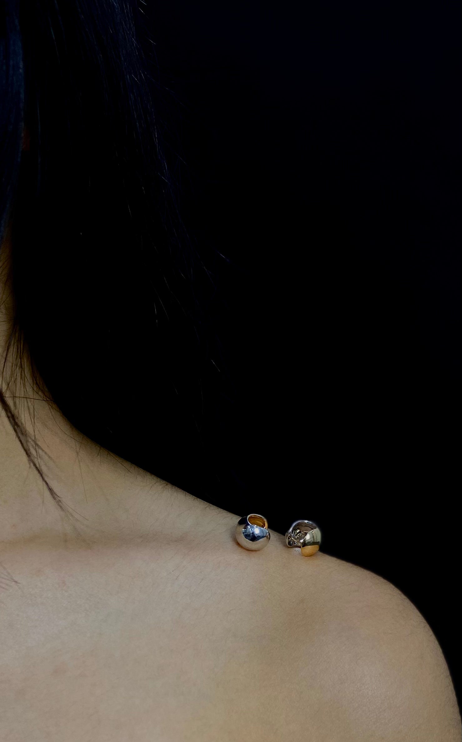 Close-up of a person wearing silver earrings against a black background.